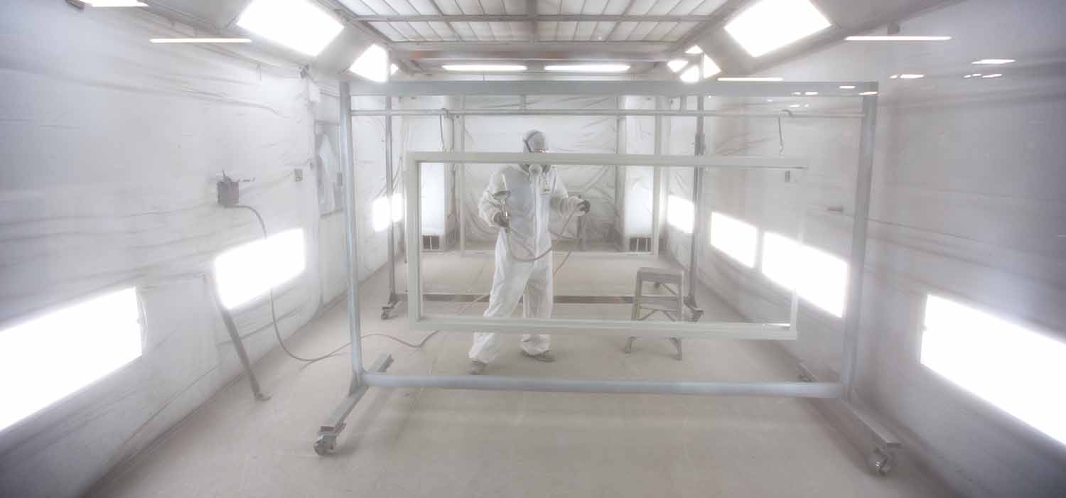 Man in paint suit and respirator in paint booth, spray painting hollow metal door and hollow metal window frames
